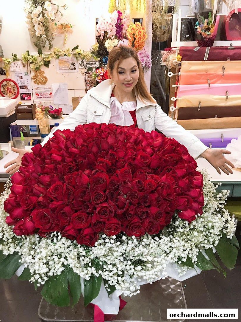A woman stands behind a large bouquet of red roses and baby's breath.