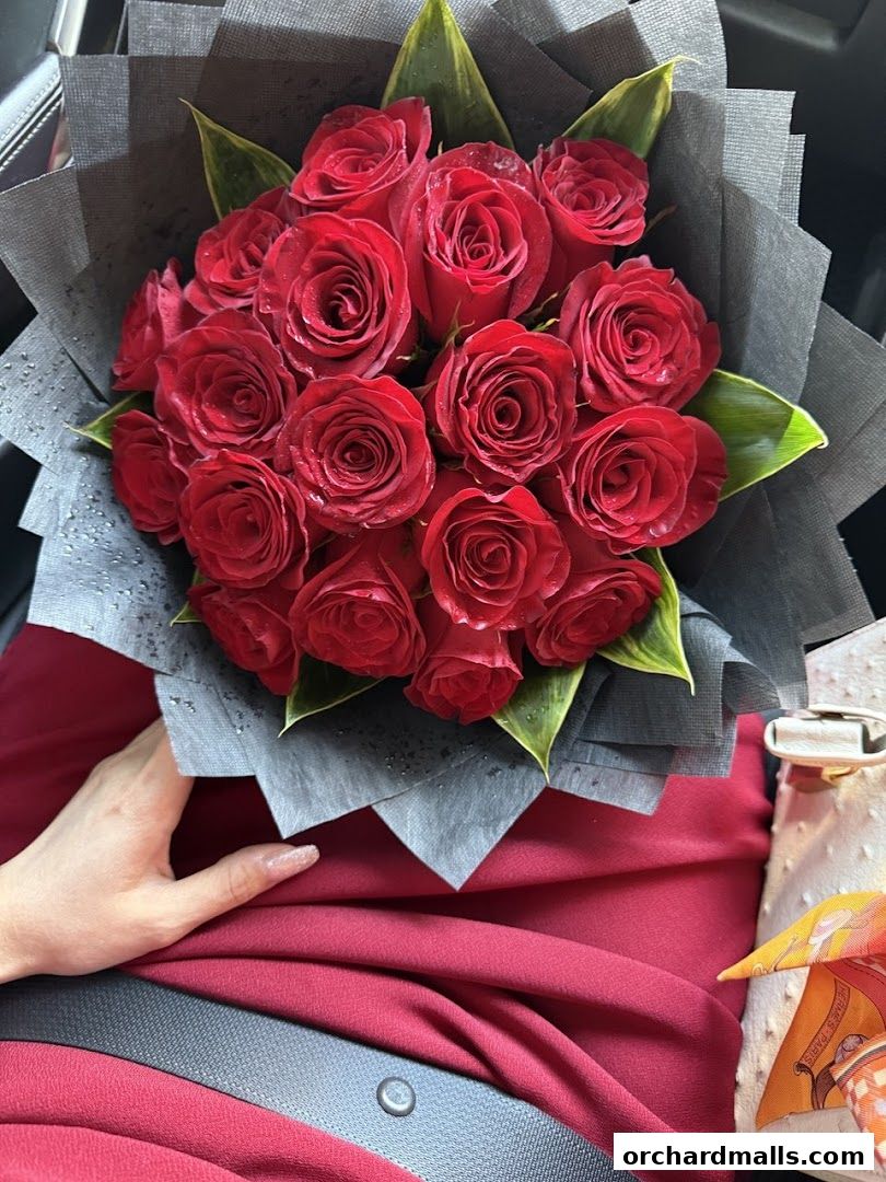 A hand holding a bouquet of red roses wrapped in black paper.