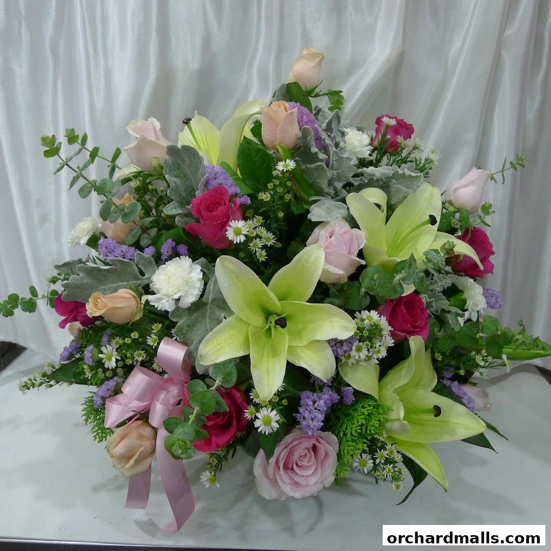 A beautiful arrangement of lilies, roses, and other flowers with a pink ribbon.