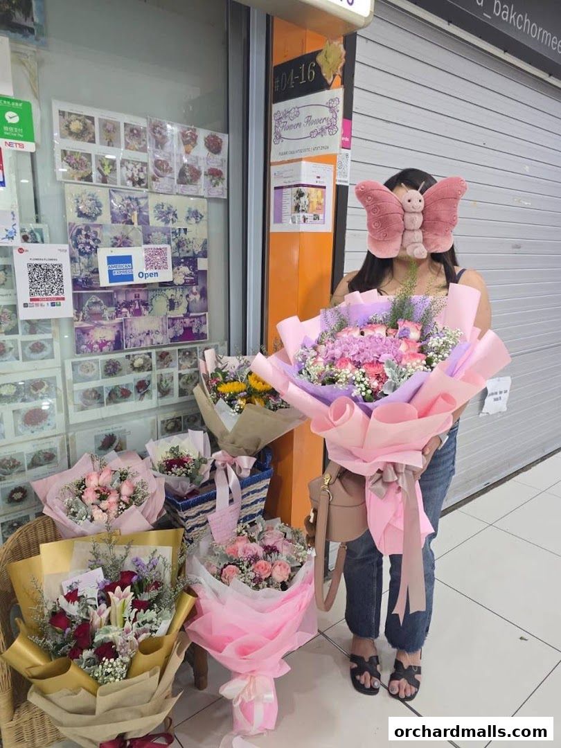 A person holds a large bouquet of flowers outside a flower shop with many arrangements displayed.