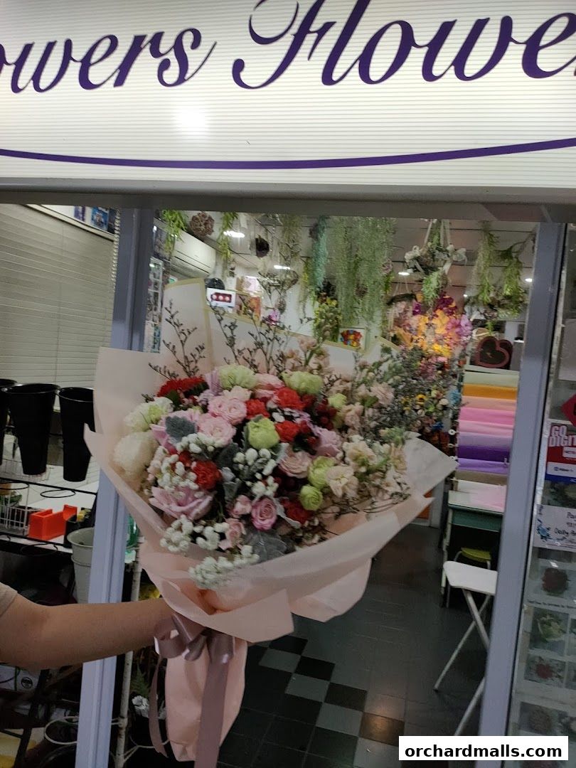 A person holds a large bouquet of flowers in front of a florist shop.