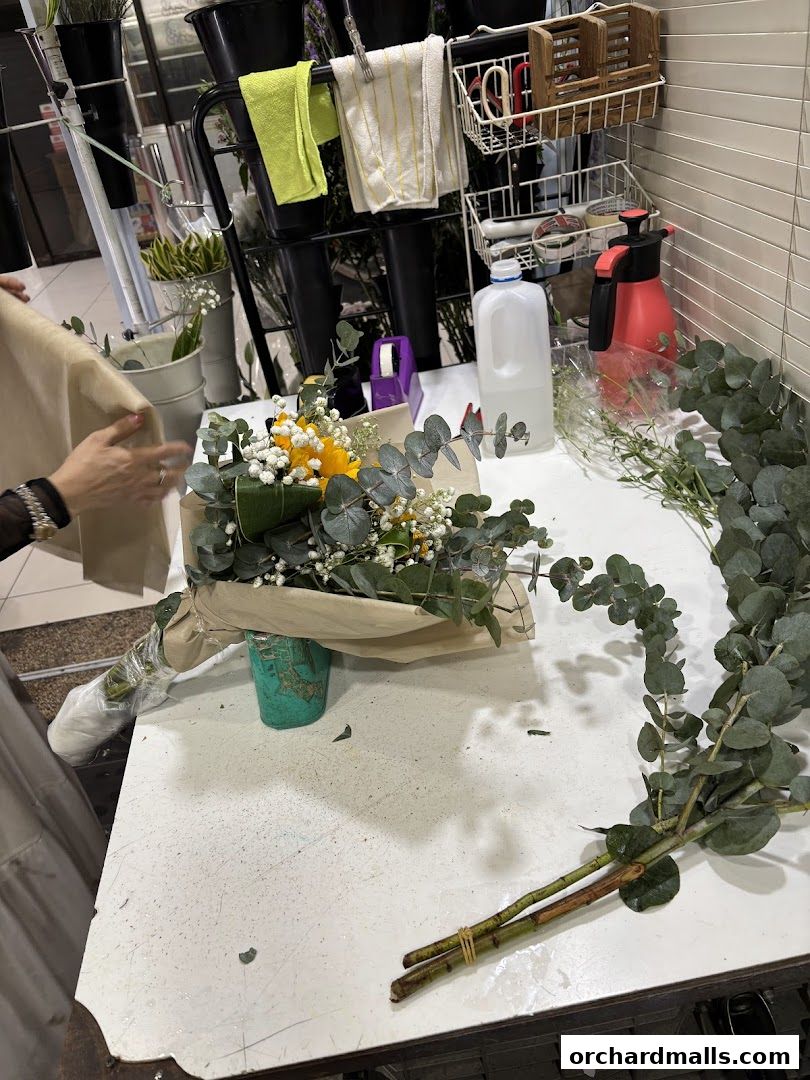 A florist is arranging a bouquet of yellow flowers and eucalyptus on a workbench.