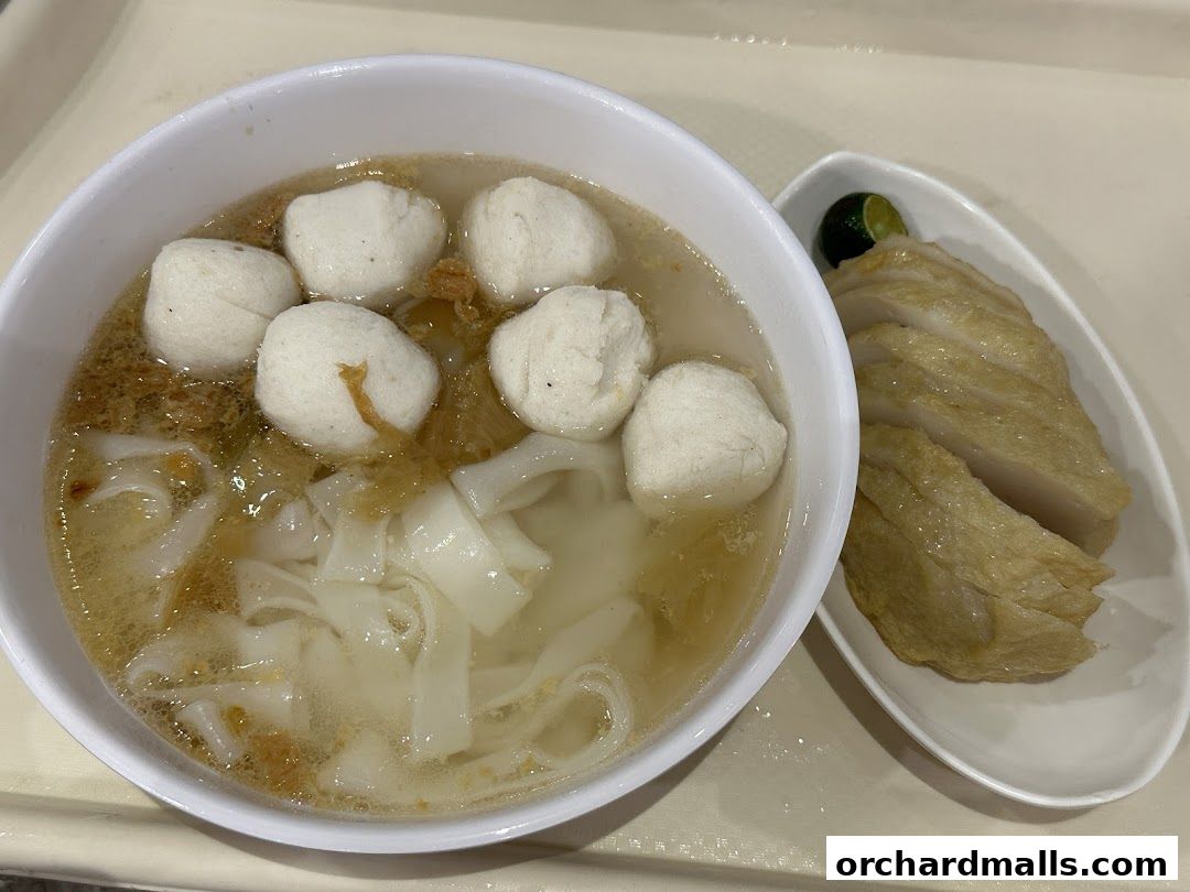 A bowl of noodle soup with fish balls and a side of sliced fish cakes with lime.