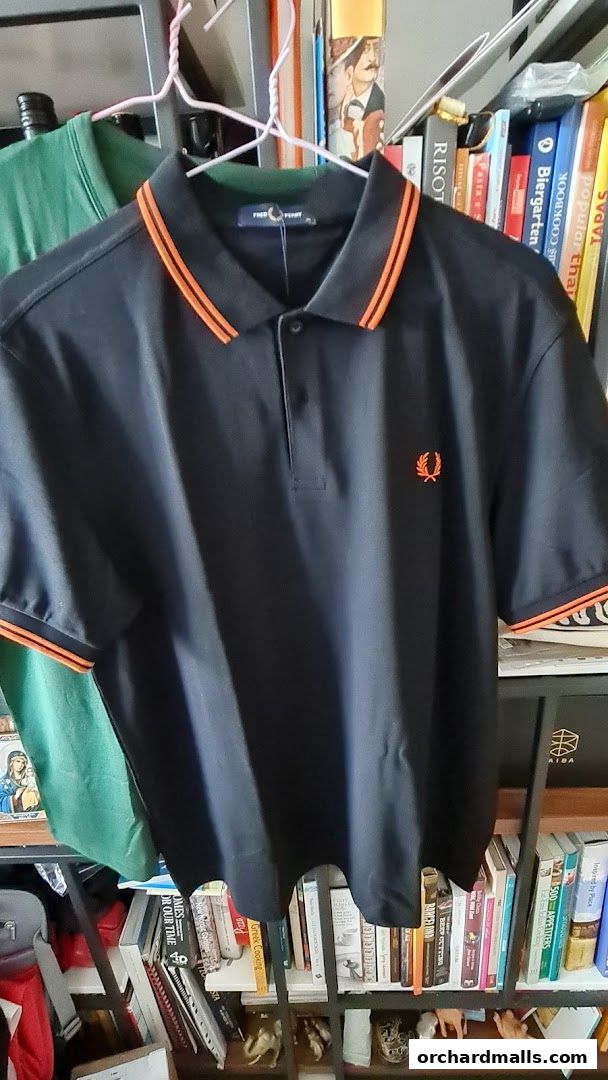 A black Fred Perry polo shirt with orange trim is displayed on a hanger.