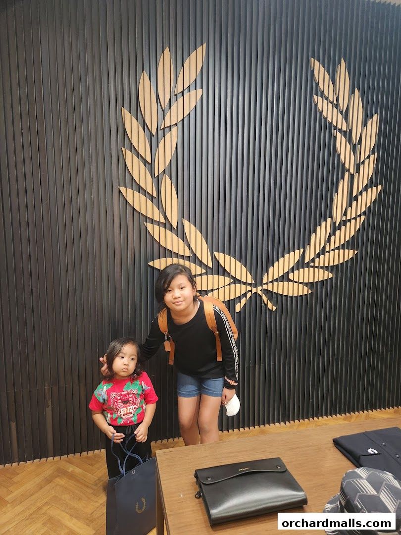 Two children pose in front of a Fred Perry store's iconic laurel wreath logo.