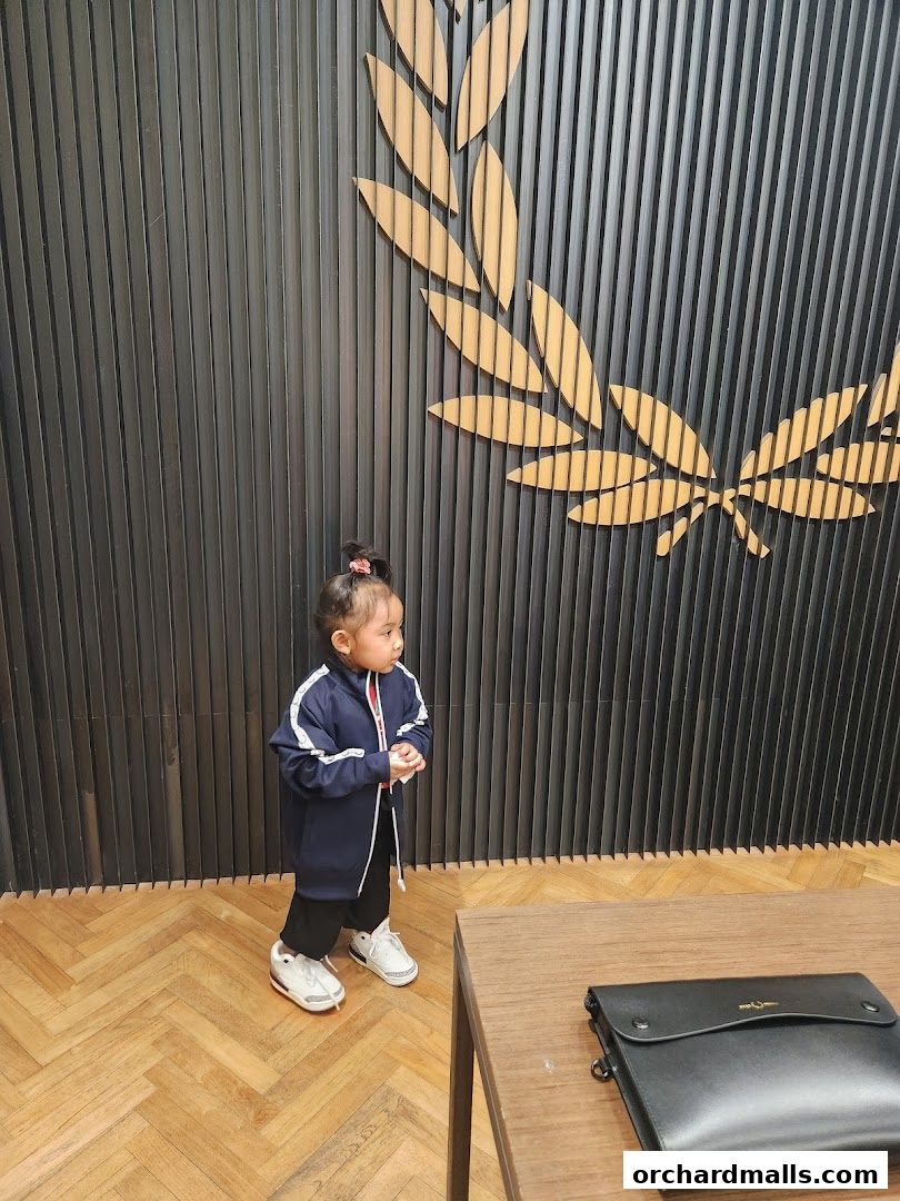 A young child stands in front of a wall with a laurel wreath design at Fred Perry.