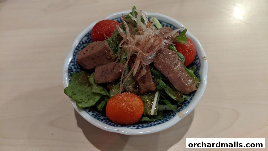 A bowl of salad with grilled meat, cherry tomatoes, and greens, topped with shredded ginger.