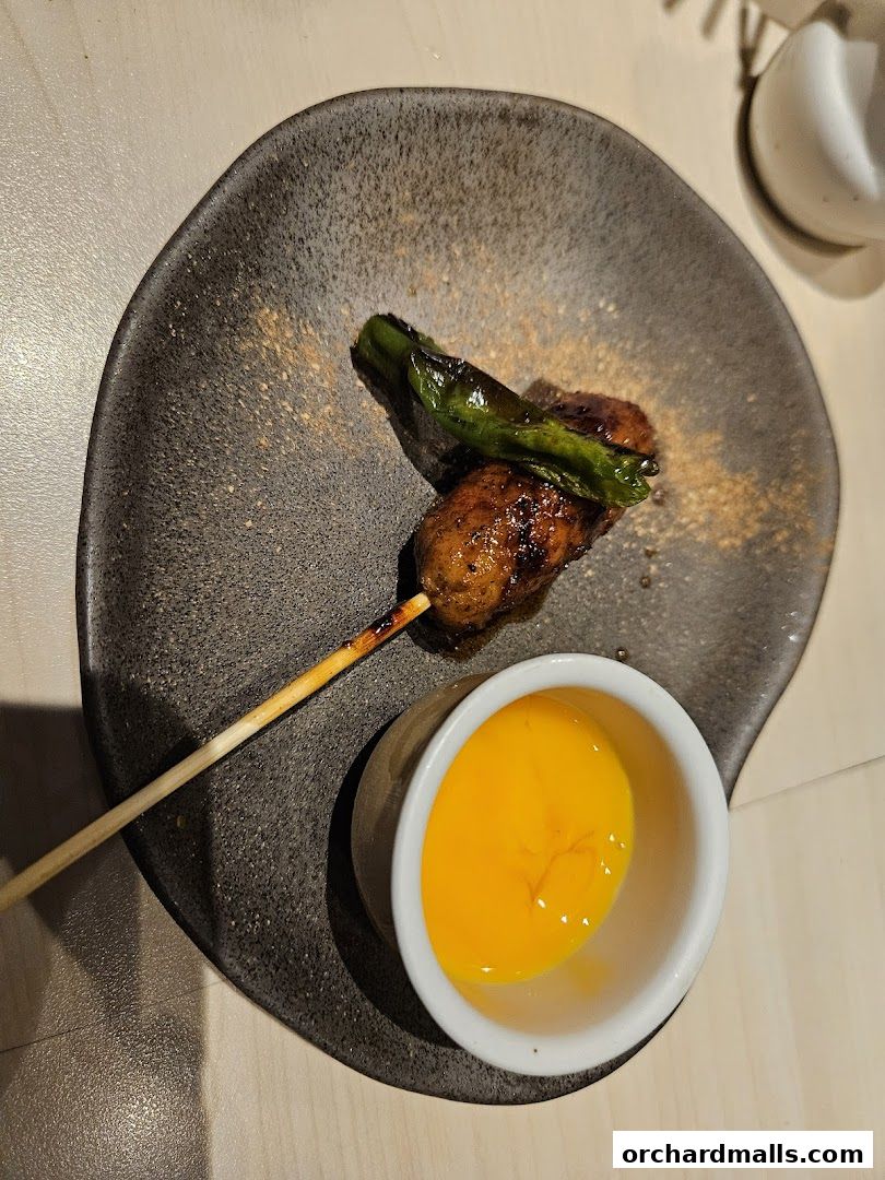 A skewer of grilled yakitori with a side of raw egg yolk dip.