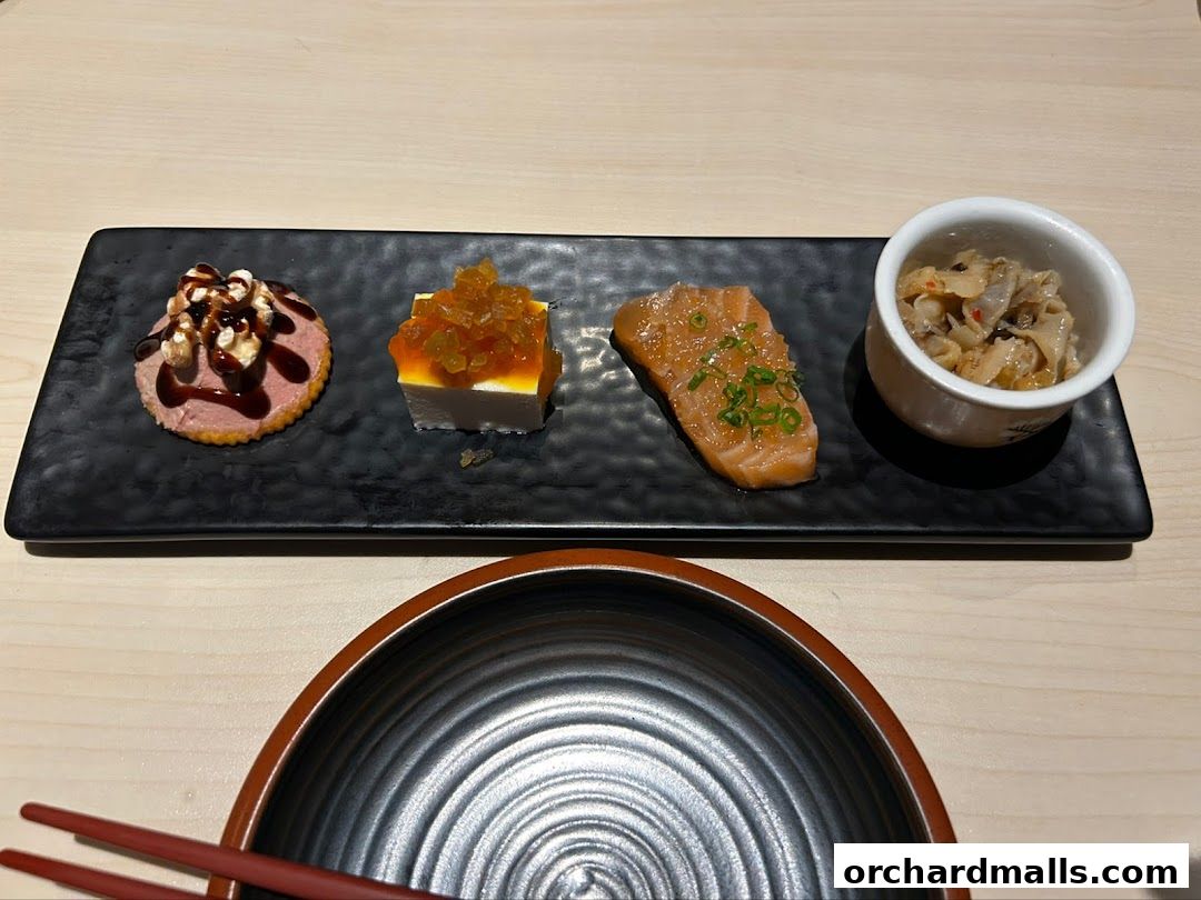 A platter of four small Japanese appetizers, including salmon and a cracker with toppings.