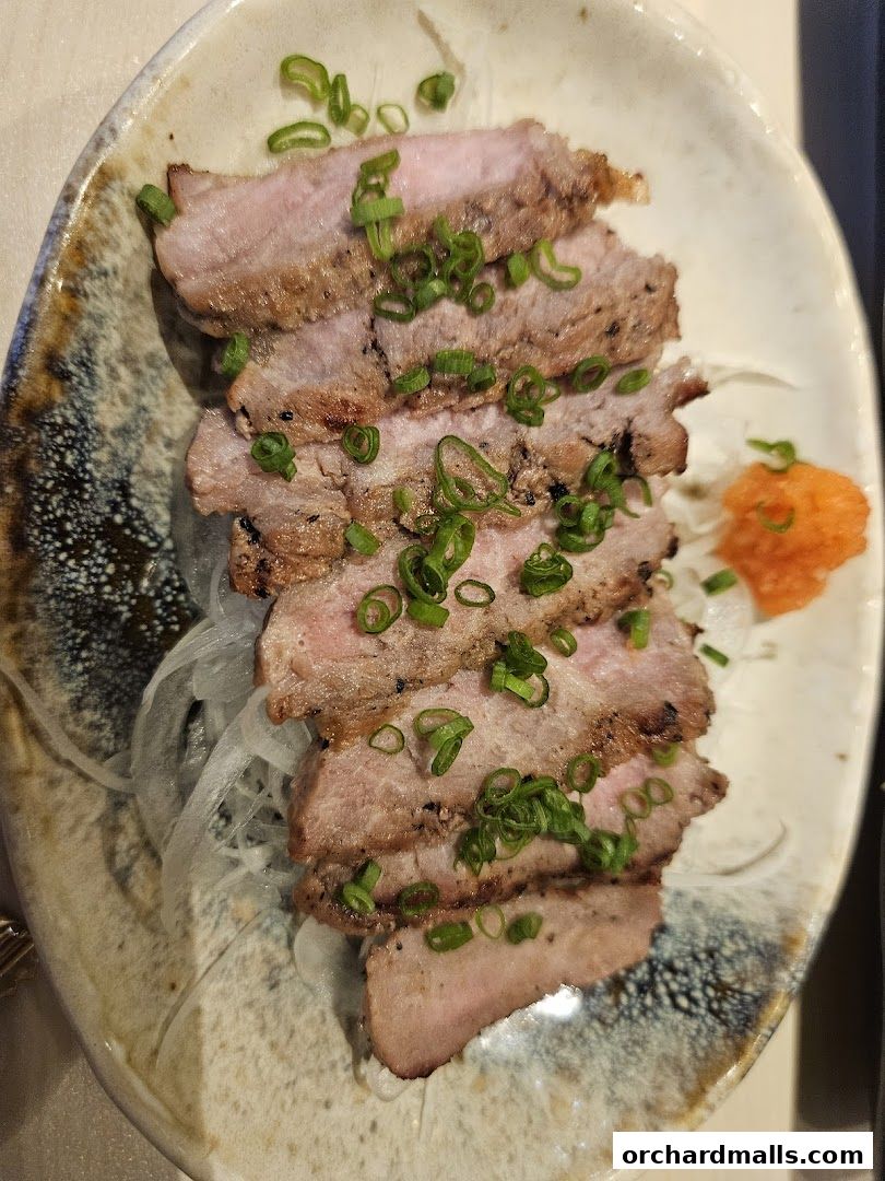 A plate of sliced grilled pork with green onions and shredded daikon.