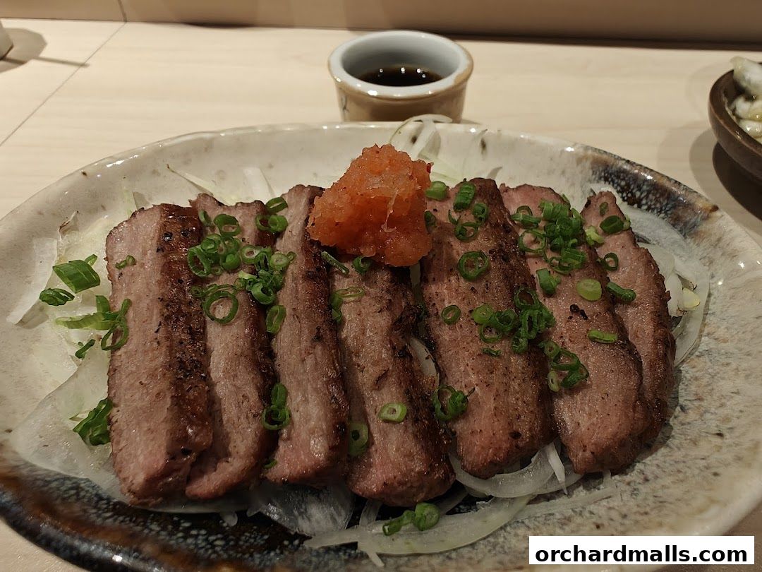 A plate of sliced grilled meat, garnished with scallions and a dollop of orange paste.