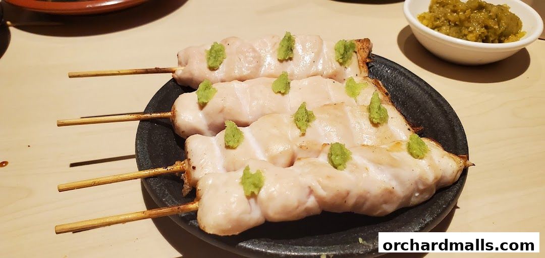 Three skewers of grilled chicken yakitori topped with green paste on a dark plate.