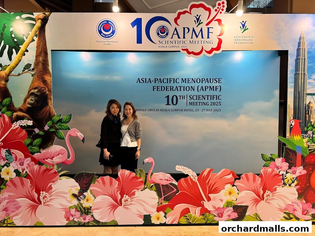 Two women pose in front of a backdrop for the 10th APMF Scientific Meeting in Kuala Lumpur.