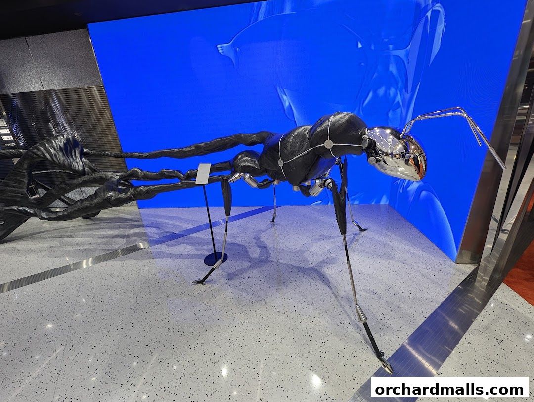 A striking metallic ant sculpture with a chrome head and black body, displayed against a vibrant blue screen.