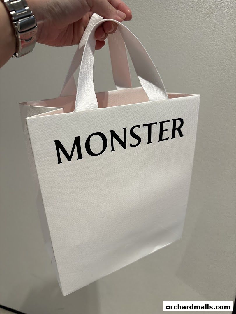 A hand holds a white shopping bag with the word 'MONSTER' printed in black.