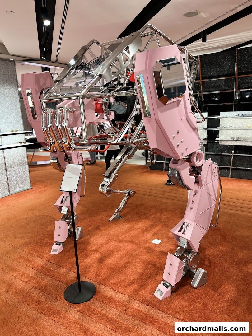 A large, pink and silver robot sculpture is displayed on an orange carpeted floor.