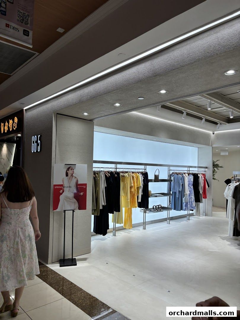 A woman walks past a clothing store displaying spring collection apparel.