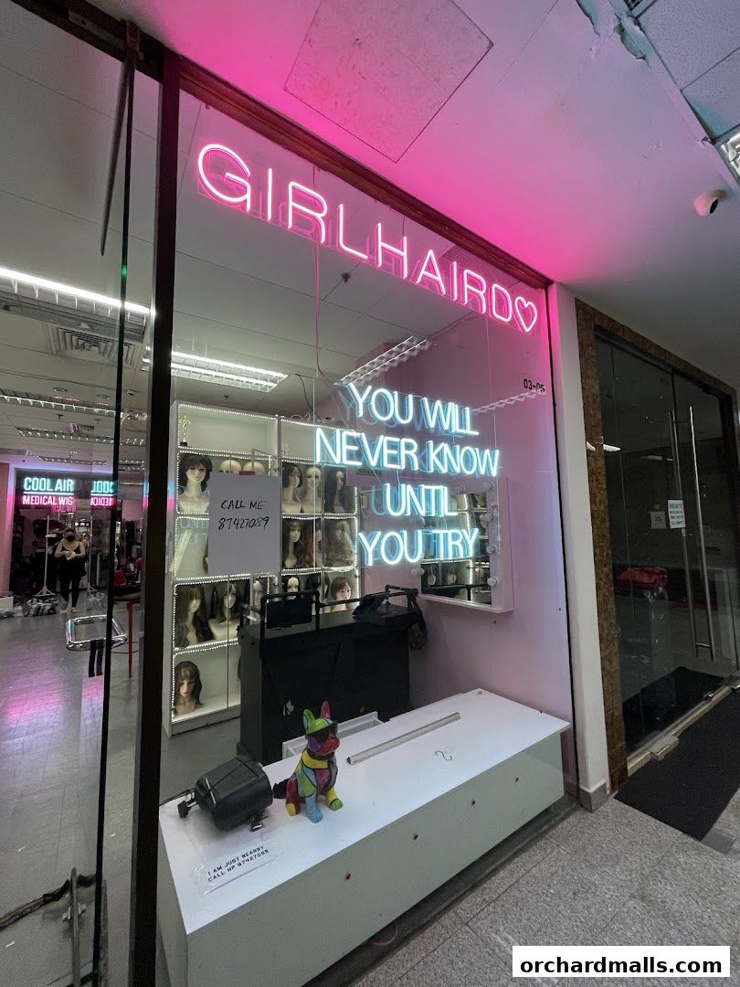 The storefront of a wig shop with neon signs and displays of wigs.