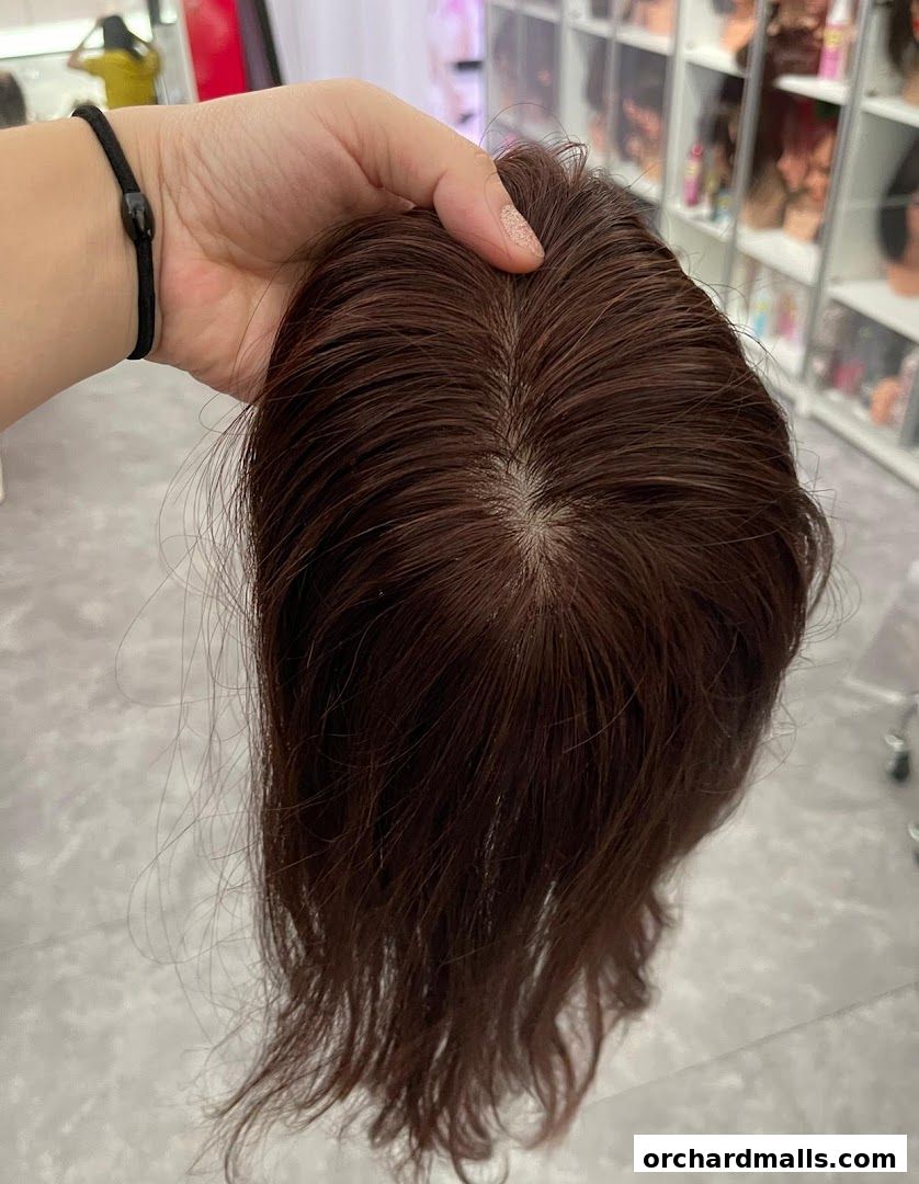 A hand holds a dark brown wig topper, showcasing its natural texture and color.