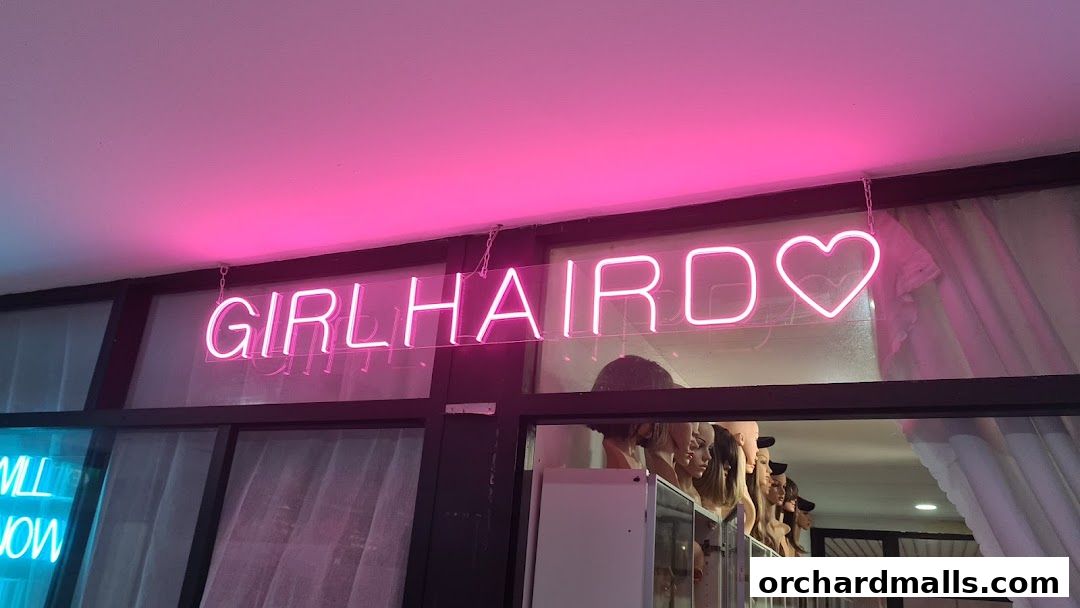 Neon sign 'GIRLHAIRDO' with a heart above mannequins displaying wigs.