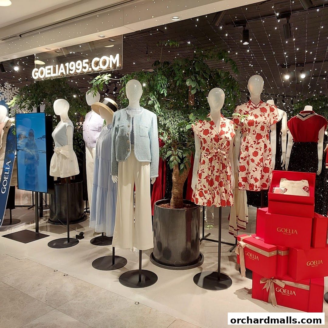 Mannequins display stylish outfits in a well-lit retail store with decorative plants and lighting.
