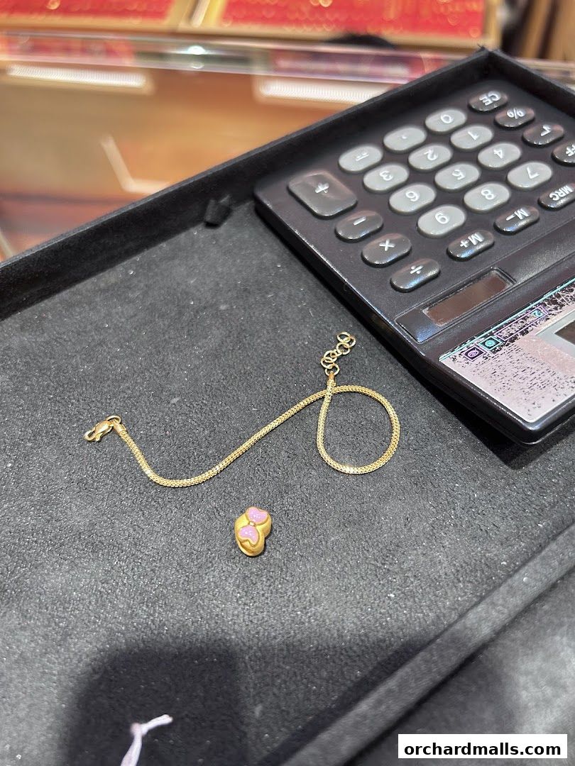 A gold bracelet with a small, pink-accented charm next to a calculator.