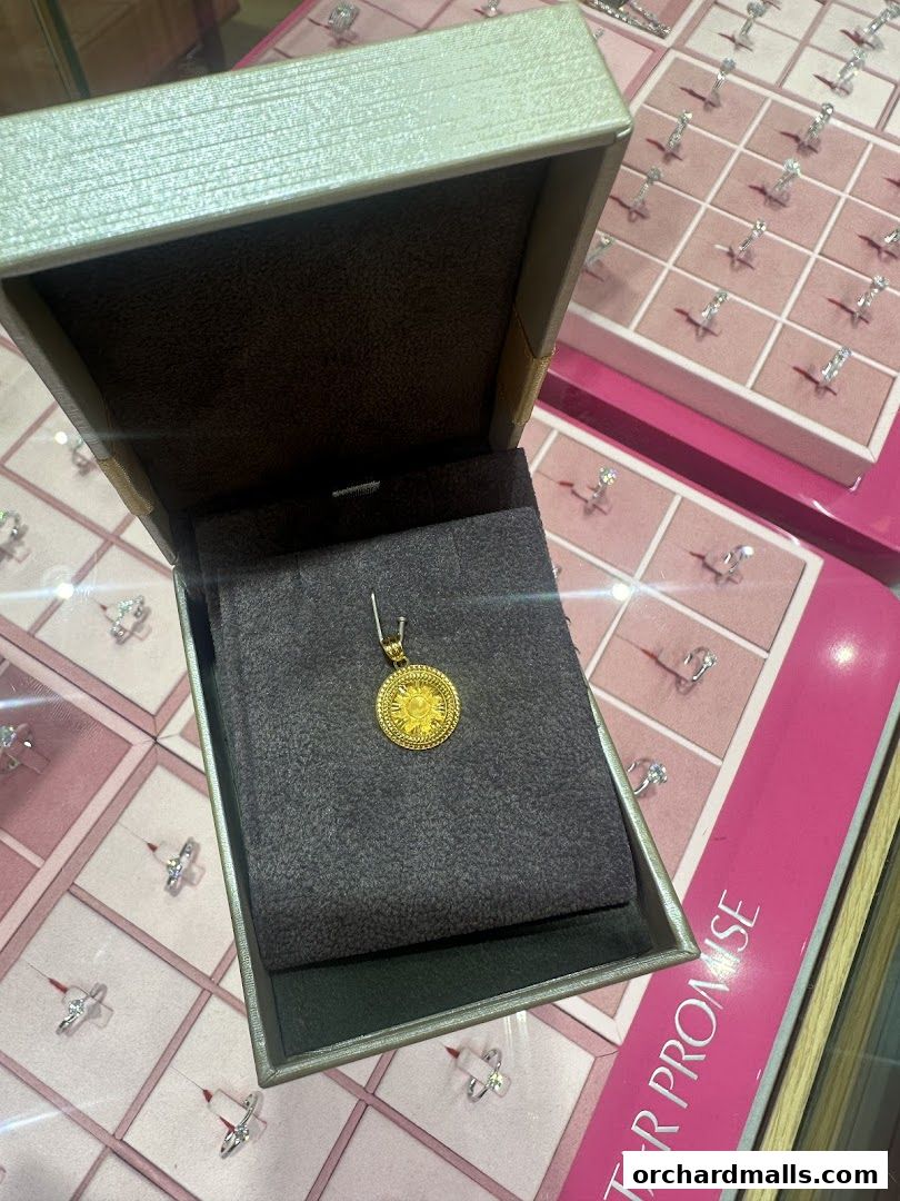 A gold pendant displayed in an open jewelry box with rings in the background.