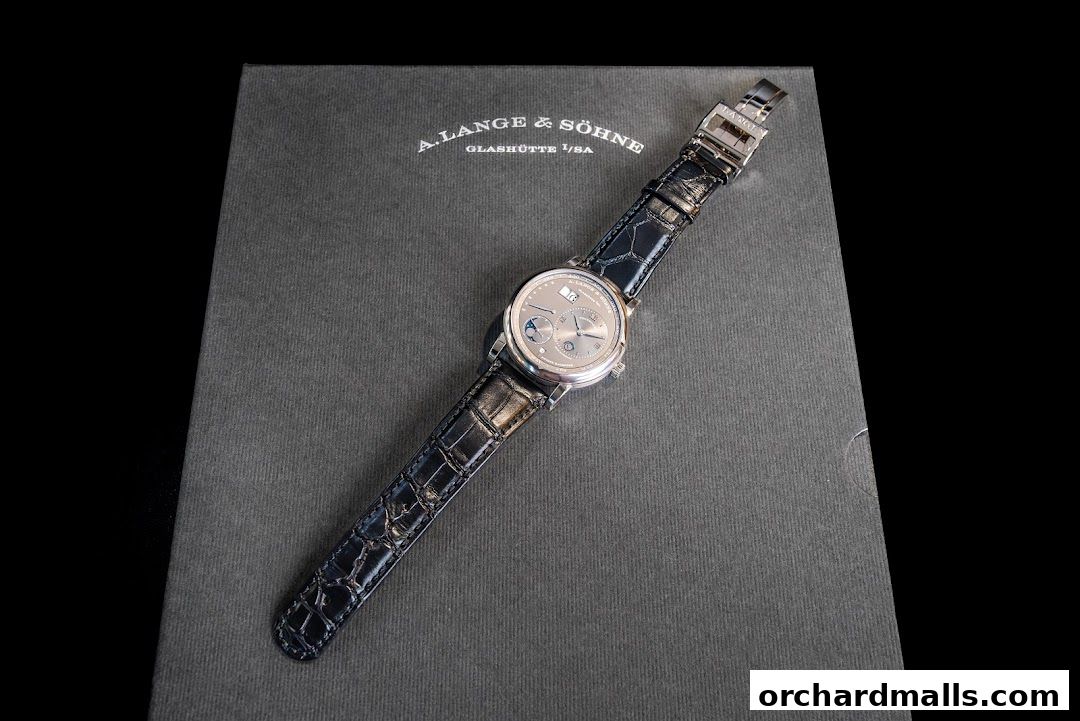 A luxury A. Lange & Söhne watch with a black alligator strap on a dark grey box.