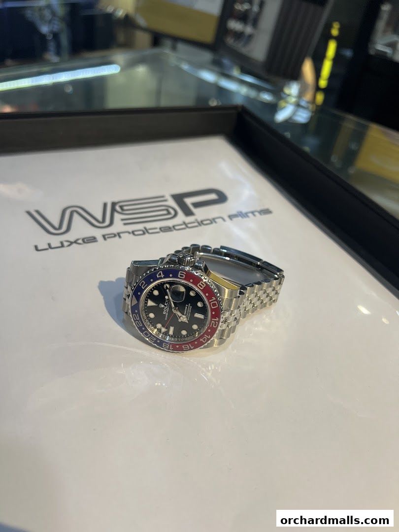 A luxury Rolex watch with a red and blue bezel displayed on a white surface.
