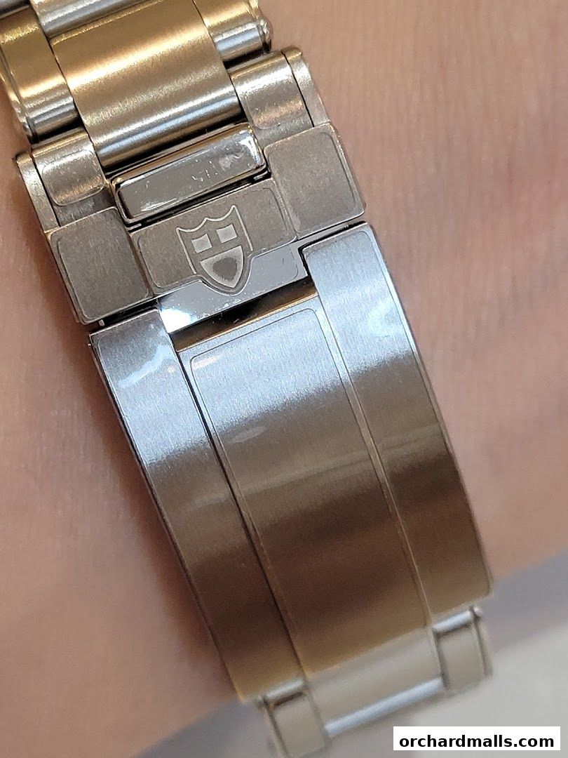 Close-up of a polished metal watch band with a shield logo.