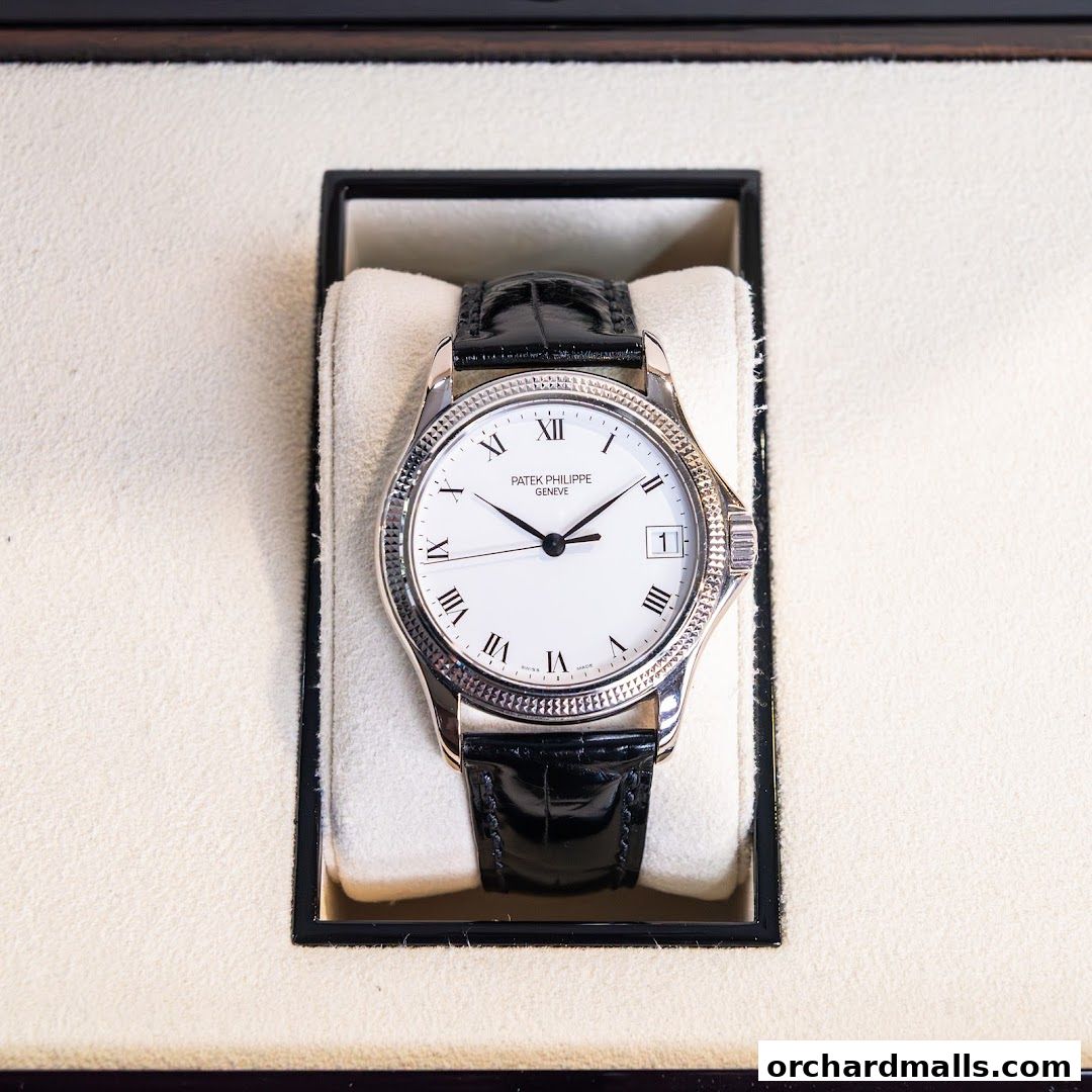 A Patek Philippe Geneve watch with a white dial and black leather strap in a display box.