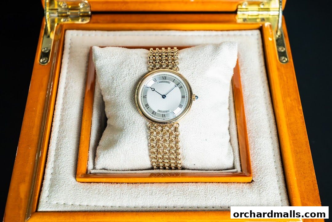 A luxurious gold watch with a white face and Roman numerals in a wooden box.