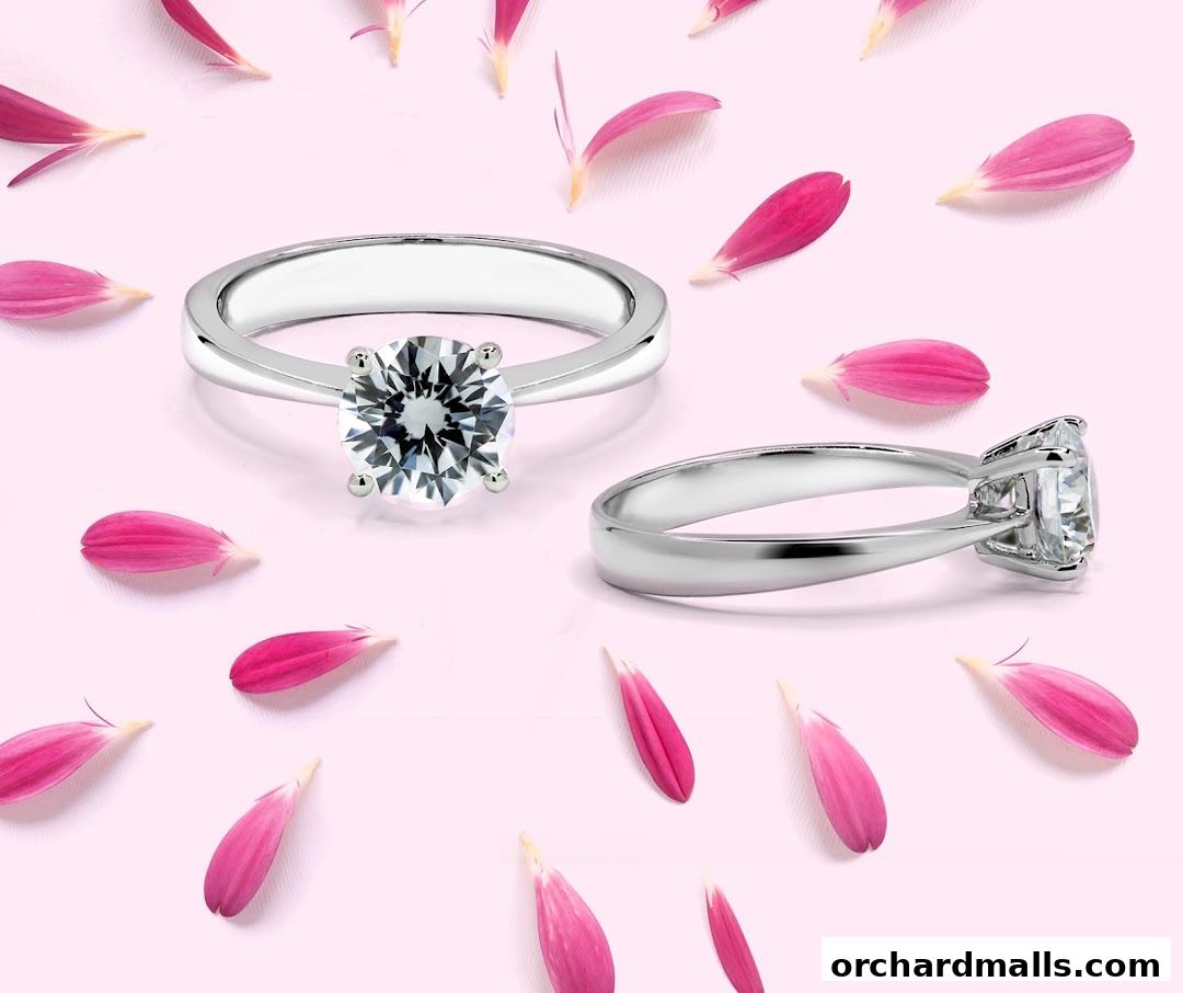 Two diamond rings are displayed with pink flower petals scattered around on a pink background.