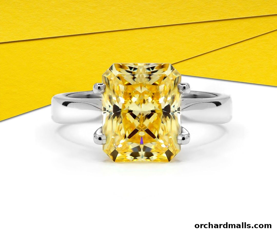 A close-up of a radiant cut yellow gemstone ring on a white surface.
