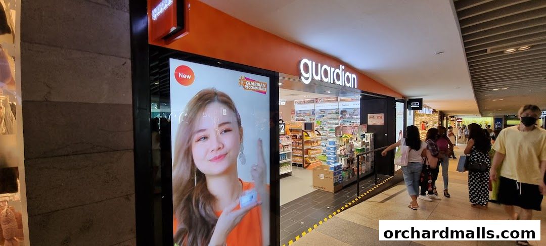 The exterior of a Guardian Health & Beauty store with a digital display and people walking by.