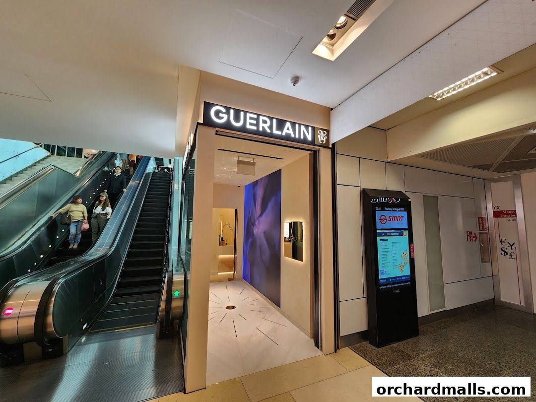The Guerlain Boutique entrance is next to an escalator in a shopping mall.