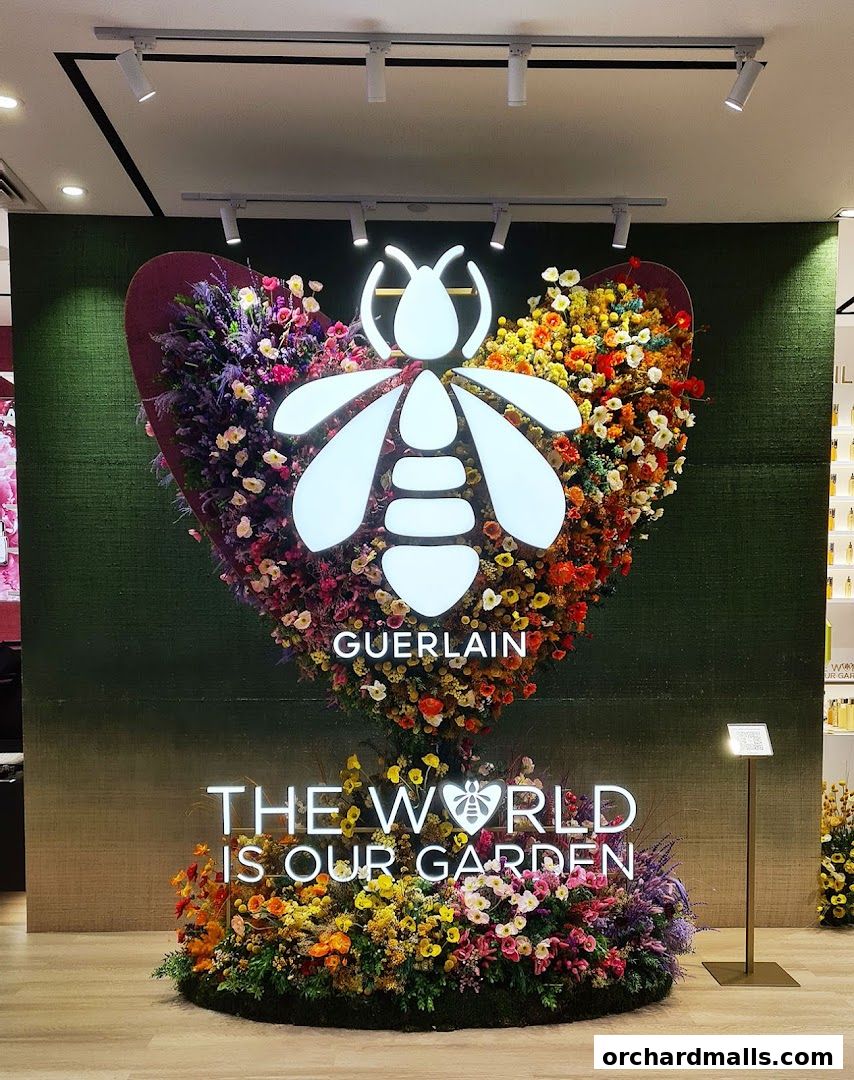 Guerlain boutique interior with a large bee logo surrounded by colorful flowers and a "The World Is Our Garden" slogan.