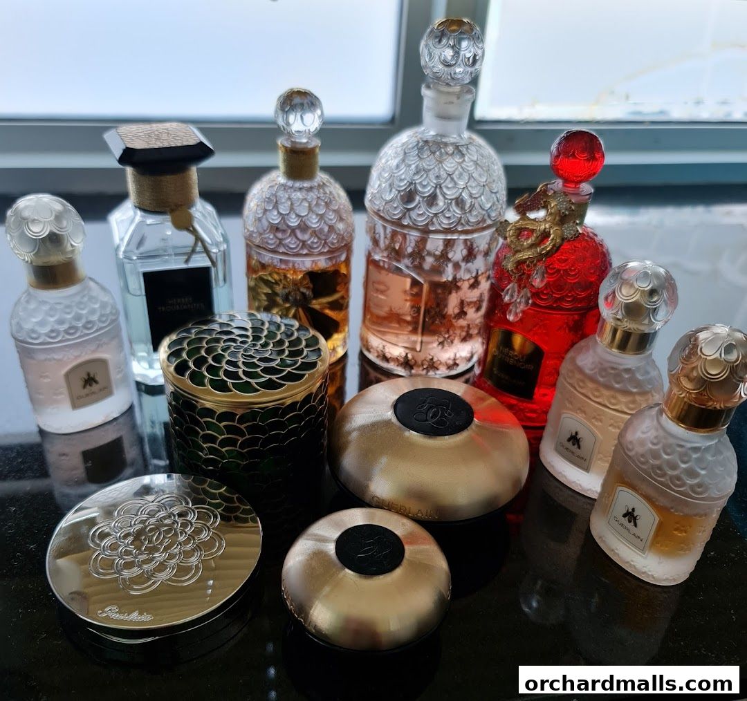 A collection of Guerlain perfumes and compacts displayed on a dark surface.
