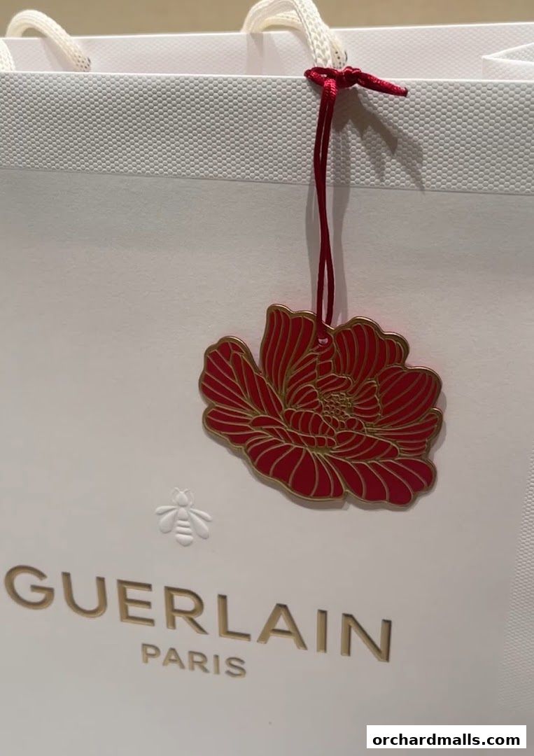 A white Guerlain shopping bag with a red floral ornament and the Guerlain Paris logo.