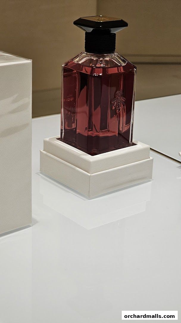 A close-up of a Guerlain perfume bottle with a red liquid and a bee emblem.