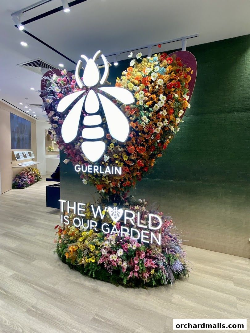 Guerlain boutique interior with a large floral display featuring the brand's bee logo and a slogan.