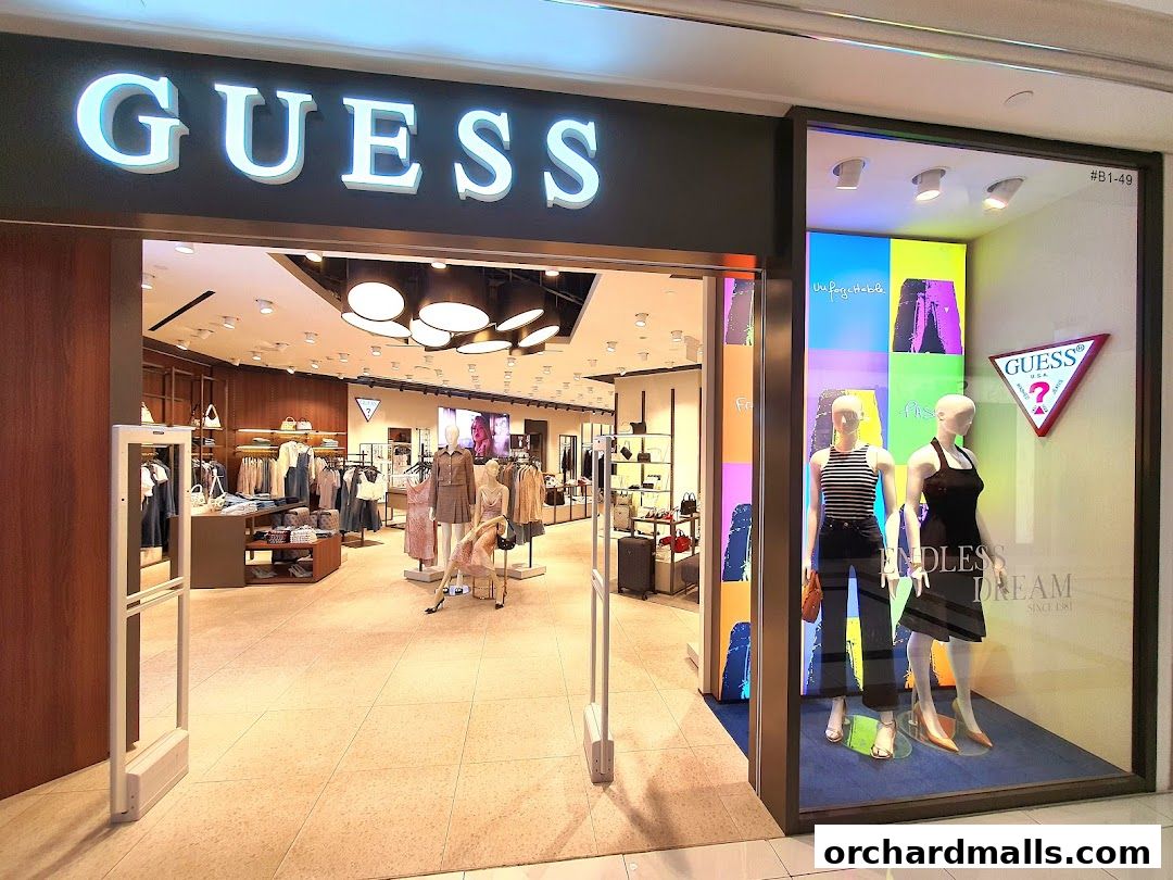 The entrance and display window of a GUESS fashion store, showcasing clothing and accessories.