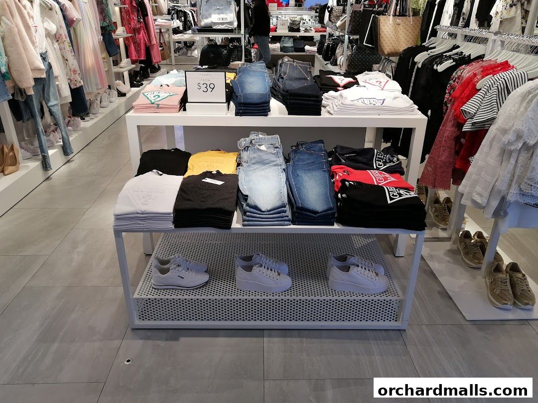 Interior view of a GUESS store showcasing folded t-shirts, jeans, and sneakers.