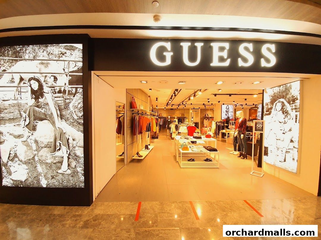 The entrance of a GUESS store, showcasing clothing displays and large black and white advertisements.