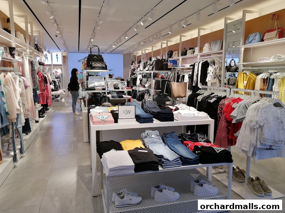 Interior view of a GUESS store showcasing clothing, handbags, and shoes on display.