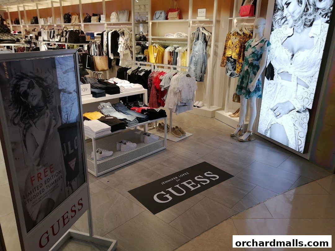 Interior view of a GUESS store showcasing clothing, handbags, and a large digital display.