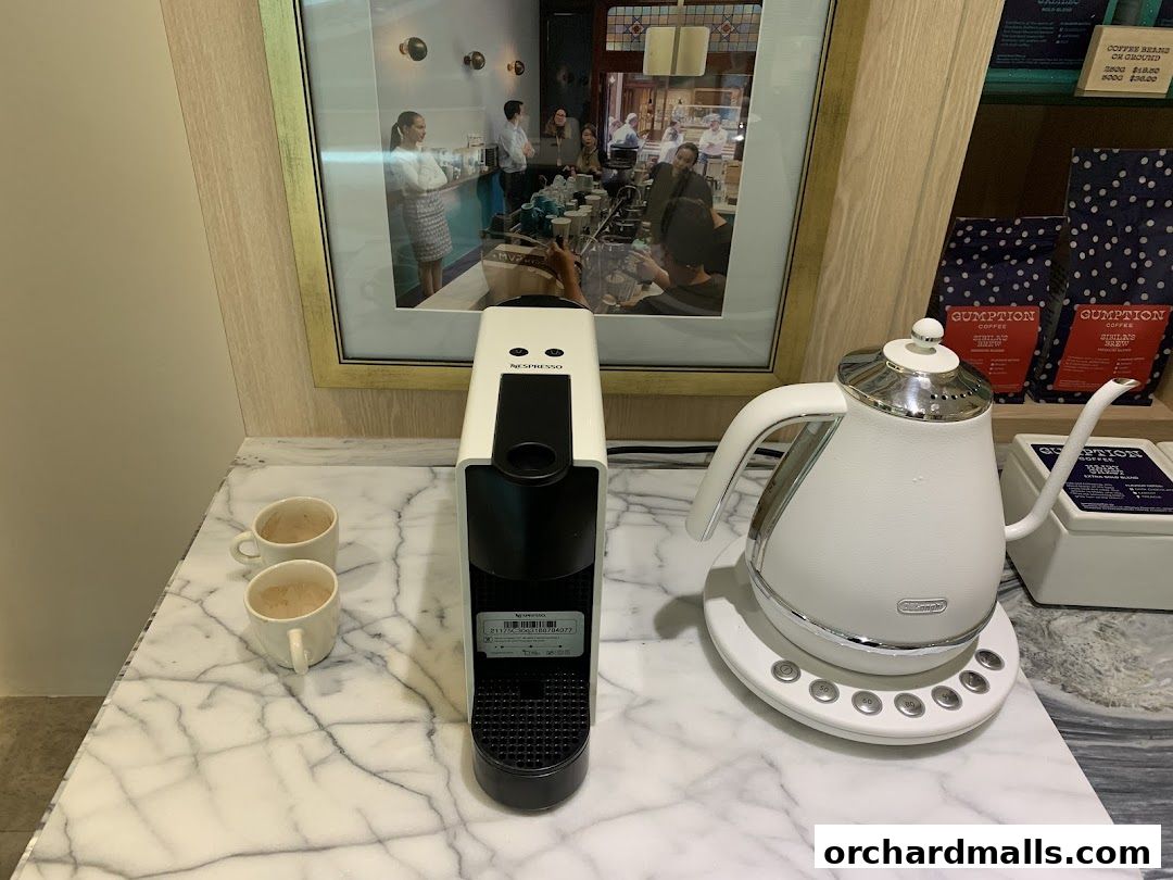 A coffee machine, kettle, and cups are displayed on a marble countertop.