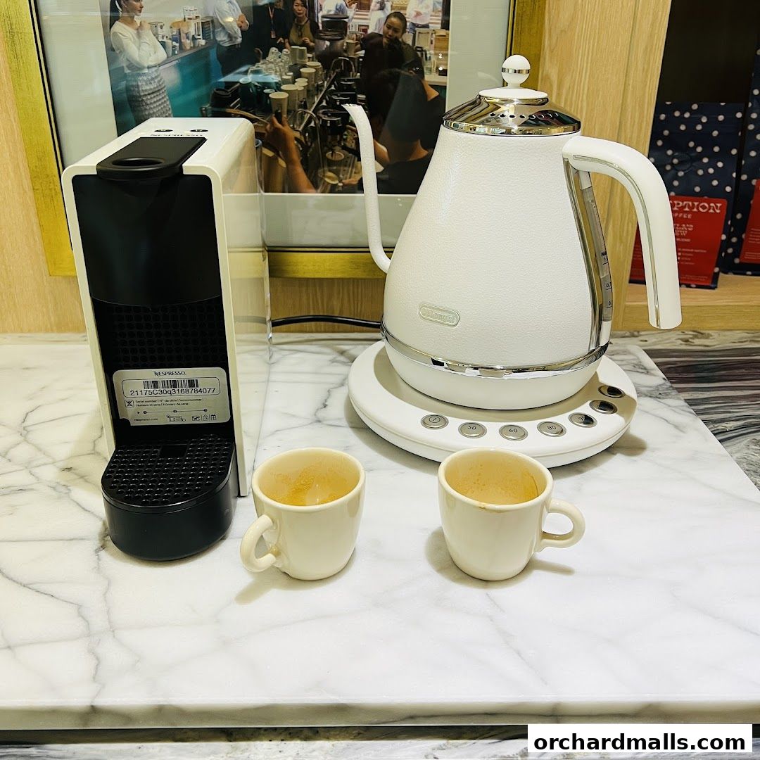 A Nespresso machine, electric kettle, and two coffee cups on a marble countertop.
