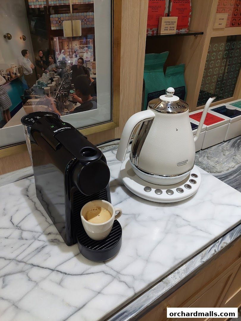 A Nespresso machine with a freshly brewed espresso and a kettle on a marble countertop.