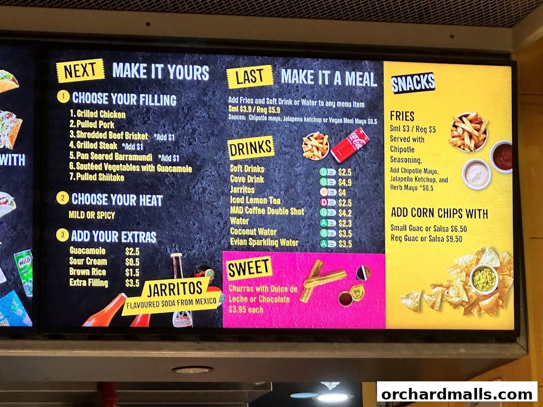 A digital menu board displaying options for fillings, heat levels, extras, drinks, snacks, and sweet items.